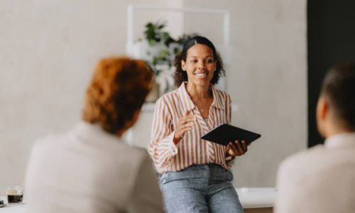 Confident businesswoman leading a group business meeting at a bright beige office. Professional interaction and teamwork concept.
