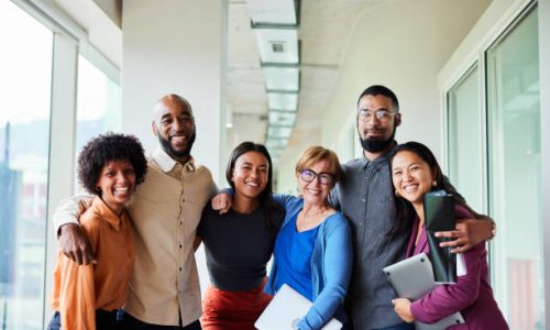 Portrait of a group of diverse businesspeople smiling while standing arm in arm together in an office corridor